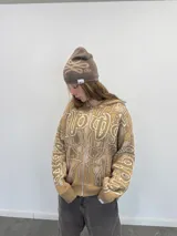 Buzo tipo hoodie con cierre frontal completo, confeccionado en tejido de punto grueso de algodón con diseño gráfico abstracto y tipográfico. Presenta capucha con bordado, puños y ruedo acanalados, y etiqueta de marca en la manga.