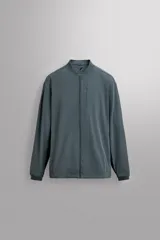 Chaqueta técnica de corte relajado, confeccionada en tejido compacto y elástico. Presenta cuello y puños acabados en rib, cierre frontal con cremallera, bolsillos frontales con cremallera oculta y bajo ajustable con elástico en los laterales.