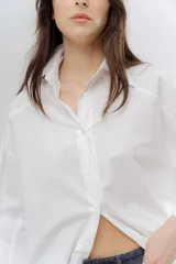 Camisa clásica de algodón con cuello camisero, cierre frontal de botones y mangas largas con puños anchos. Presenta un corte holgado y diseño minimalista.