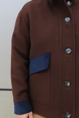 Campera de paño de lana en color beige jaspeado, con diseño oversize. Presenta detalles en pana color marrón chocolate en los puños y en las tapas de los bolsillos frontales. Cuenta con cierre frontal de botones grandes y cuello alto.