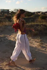 Pantalon de lino color blanco, de corte holgado y estilo babucha, con detalles de franjas estampadas en los laterales y cordones ajustables en los tobillos.