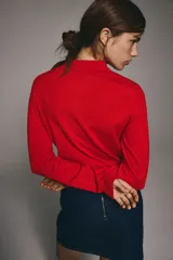 Sweater de punto fino color rojo, manga larga con hombros ligeramente caídos, cuello polo y tapeta de botones. Presenta remates acanalados en puños y bajo.
