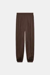 Pantalón de tiro alto con diseño abullonado, confeccionado en tejido satinado con acabado plisado y puños elásticos en los tobillos.