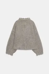 Chaqueta estilo bomber de punto color gris, con cuello subido, manga larga y acabados elásticos con frunces en puños y cuello. Cierre frontal con botones a presión ocultos.