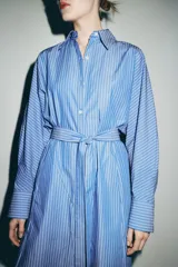 Vestido midi de corte camisero con estampado de rayas verticales, cuello solapa, manga larga con puños y cierre frontal con botones. Incluye un cinturón de lazada en el mismo tejido y bolsillos laterales ocultos.