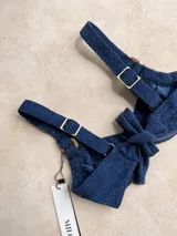 Top de bikini con aros, confeccionado en tela brillante color azul oscuro. Presenta breteles regulables con argollas decorativas y cierre mediante atado en la espalda.