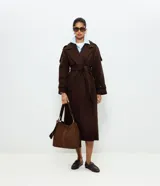 Trench coat marrón oscuro de corte largo, confeccionado en tejido polyvelour, con solapas amplias, mangas largas con trabillas en los puños, solapas en los hombros y cinturón ajustable para anudar en la cintura.
