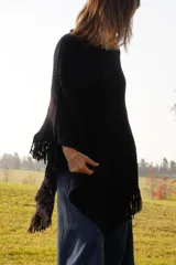 Poncho tejido en lana merino color marrón, con diseño de punto acanalado y terminación con flecos en el borde inferior. Incluye una pequeña etiqueta de cuero en la parte posterior.
