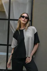 Remera de tejido de punto, manga corta, con diseño bicolor en negro y beige. La prenda es de corte holgado y presenta un ligero acanalado vertical.