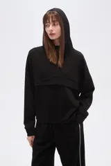 Buzo negro de corte holgado con capucha, manga larga y bolsillo frontal tipo canguro. Presenta un diseño minimalista con una solapa frontal sobre el pecho.