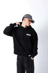 Hoodie negro de frisa con capucha y bolsillo canguro. Presenta un aplique rectangular en el pecho con texto en verde lima.