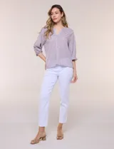 Blusa de gasa de color lila con calce holgado, cuello a la base con escote en V y cartera de botones a tono. Cuenta con fruncidos en el cuello y hombros que otorgan volumen, manga tres cuartos estilo abullonado con puño elastizado y ruedo suavemente redondeado.