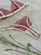 Conjunto de lencería compuesto por un corpiño triangular de encaje y una bombacha tipo tanga a juego. Ambas piezas presentan encaje en tono rosado con detalles de terminaciones en color crema.