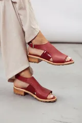 Sandalias de cuero color bordó, con capellada ancha, tira de talón regulable con hebilla metálica y suela track con taco bajo de madera.