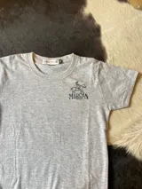 Remera de manga corta color gris melange, con cuello redondo y diseño bordado en el pecho con la leyenda "Marcha Funcional S.C.C.C.U." y la figura de un jinete a caballo.