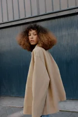 Chaqueta de corte recto y estilo camisero en color beige, con cuello solapa, manga larga y cierre frontal con botones. Presenta dos bolsillos delanteros de plastrón.