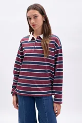 Remera de manga larga estilo rugby, con cuello polo blanco y tapeta de botones. Presenta un patrón de rayas horizontales anchas en color bordó y azul marino, separadas por finas líneas blancas.