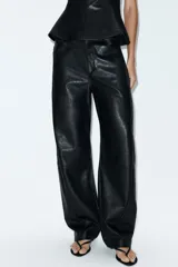Pantalón de tiro medio confeccionado en material efecto piel color negro. Presenta corte recto, bolsillos laterales y traseros, y detalle de pliegues en el frente. Cierre frontal con cremallera y gancho metálico.