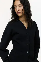 Blazer negro de punto grueso, corte entallado con hombros caídos, escote en V, cierre frontal de botones y bolsillos insertados decorativos.