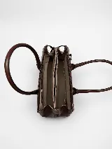Cartera de mano estructurada de cuero vacuno rojo, con doble asa superior y detalles de charol en la parte superior. Cuenta con cierres metálicos y apliques decorativos laterales con hebillas.