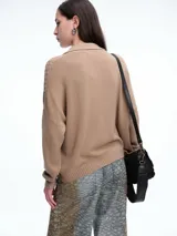 Sweater de tejido de punto color beige, con diseño de trenzas en el frente y mangas lisas. Presenta cuello polo con escote en V y puños y ruedo acanalados.