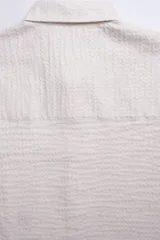 Camisa de manga corta color crema con textura, botones de madera y parche con logo.