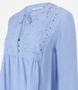 Blusa tipo bata de color celeste con mangas largas y cuello mao con lazo. Presenta detalles de bordado floral calado tipo laise en el frente y cierre parcial con botones.
