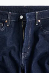 Jeans de cinco bolsillos en denim de algodón con leve stretch, color azul oscuro. Modelo de corte ajustado de cintura a muslo, más holgado de rodilla a bajo, con pierna acampanada (corte para bota) y tiro alto con cierre y botón.
