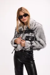 Campera de pelo sintético negro con detalles en cuero sintético, bolsillos frontales con solapa y cinturón ajustable con hebilla metálica.