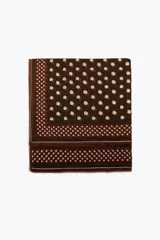 Pañuelo cuadrado de mezcla de tejidos y lana, color marrón oscuro con estampado de lunares beige. Presenta un borde con franjas y lunares más pequeños, y terminaciones deshilachadas.