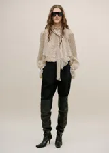Blusa de gasa color beige con estampado de lunares negros, cuello alto con lazo integrado y mangas largas con puños amplios.
