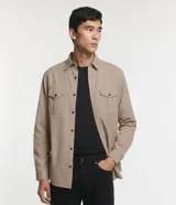 Camisa de manga larga confeccionada en sarga de algodón, con cuello clásico, cierre frontal abotonado y dos bolsillos frontales con solapa y botón.