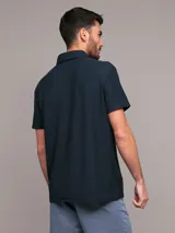 Chomba de manga corta Calvin Klein color azul marino, con cuello polo y cierre frontal parcial con cremallera. Presenta una banda horizontal en el pecho con el logo de la marca bordado.
