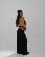 Vestido largo negro de corte ajustado, con escote profundo en V y espalda descubierta. Presenta un tajo lateral en la falda y un detalle de textura brillante en el borde del escote.