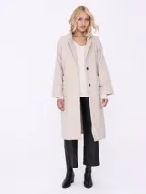 Tapado largo color beige con cuello solapa, cinturón y mangas largas con detalle matelassé.