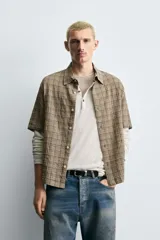 Camisa de algodón con textura arrugada, corte relaxed fit, color beige con patrón de cuadros en tonos marrones y negros. Posee cuello bowling y manga corta.