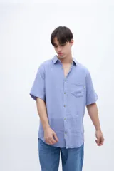 Camisa de manga corta color celeste claro, con cuello solapa clásico y bolsillo en el pecho. Presenta una textura ligera y un calce regular.