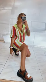 Vestido corto tejido calado a rayas horizontales en tonos naranja, amarillo y blanco, con cuello tipo polo y cierre frontal con botones.