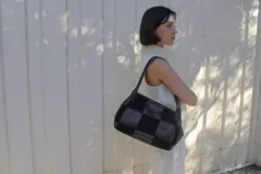 Cartera de hombro con diseño de patchwork que alterna paneles de cuero liso y gamuza en color marrón oscuro. Presenta doble asa trenzada y estructura rectangular.