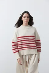 Polera de tejido de punto con diseño a rayas horizontales en color azul marino sobre base beige. Presenta cuello alto, mangas largas con puños acanalados y una silueta relajada.