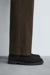 Bota estilo Chelsea de hombre, confeccionada en piel con acabado de serraje en color marrón. Presenta elásticos laterales oscuros para facilitar el calce, horma redonda y suela a tono con un ligero tacón.