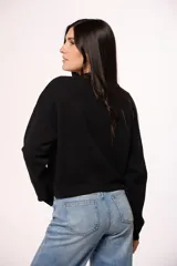 Buzo tejido de punto color negro, con cuello redondo, mangas largas y detalle de corazón bordado con brillos en el pecho.