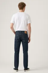 Pantalón de jean corte slim taper, de color azul oscuro con costuras en contraste. Presenta diseño de cinco bolsillos, cierre de botón y bragueta con cremallera.