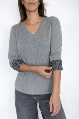 Sweater de punto con escote en V y manga larga. Presenta un diseño exterior liso en color gris, con un detalle distintivo de animal print en el interior de los puños, visible al doblarlos.