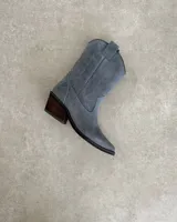 Bota corta de gamuza color marrón topo, estilo western, con bordados decorativos en hilo blanco en caña y empeine. Posee taco cuadrado de madera y punta ligeramente afilada.