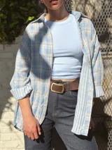 Camisa de corte oversize, con estampado a cuadros en tonos celeste, blanco y beige, cuello camisero, cierre frontal con botones y bolsillo aplicado en el pecho.