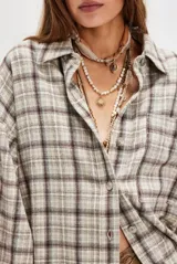 Camisa de franela de algodón con estampado a cuadros en tonos beige, blanco y marrón oscuro. Presenta un corte amplio y holgado, cuello camisero y botones frontales.