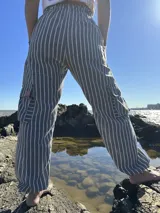 Pantalón de tela gris con rayas verticales blancas, corte holgado, cintura elástica y bolsillos cargo laterales.