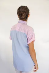 Camisa de manga corta con diseño de rayas en tonos rosa, celeste, verde y blanco. Cuenta con cuello camisero, cierre frontal con botones y un bolsillo en el pecho.