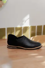Zapato tipo mocasín de diseño bicolor, con puntera en cuero texturizado efecto cocodrilo y talón en gamuza negra. Presenta cierre trasero y suela plana con detalle de vira en tono natural.